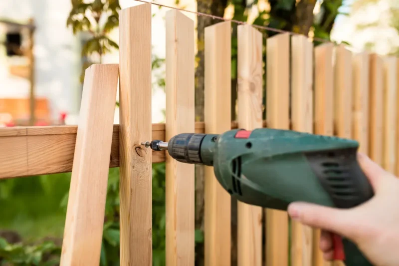 A gardener repairing a wooden fence in a garden
